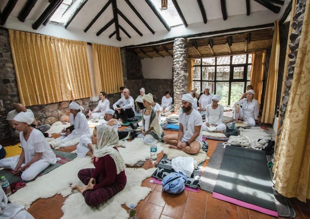 A group of people sitting on mats in a rustic room with stone walls and wooden beams.