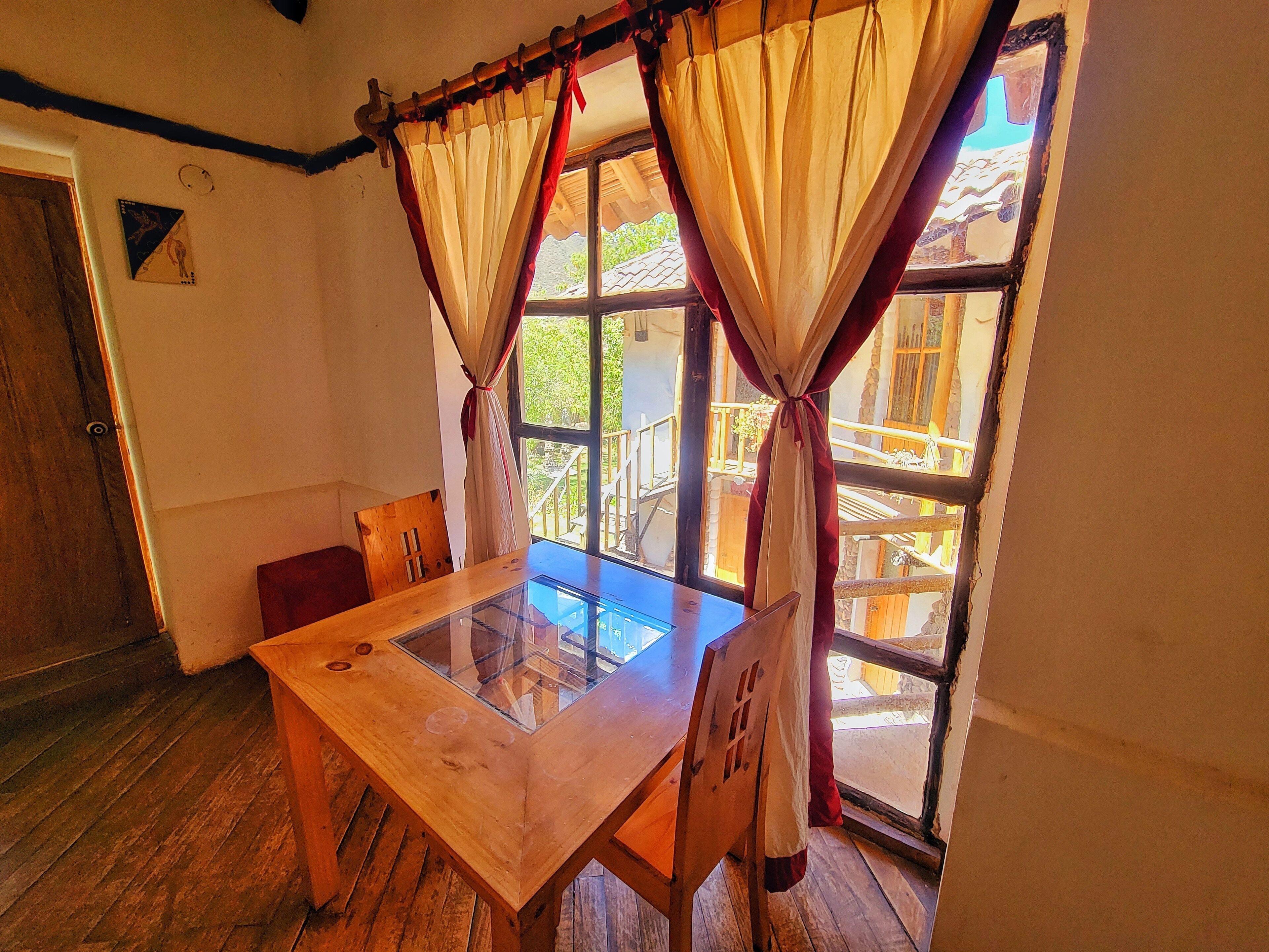 Una mesa de madera con cubierta de vidrio, ubicada cerca de una ventana con cortinas.
