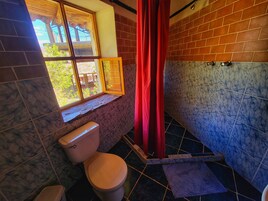 Un baño con inodoro, una ventana con vistas, una cortina roja y suelo de baldosas.