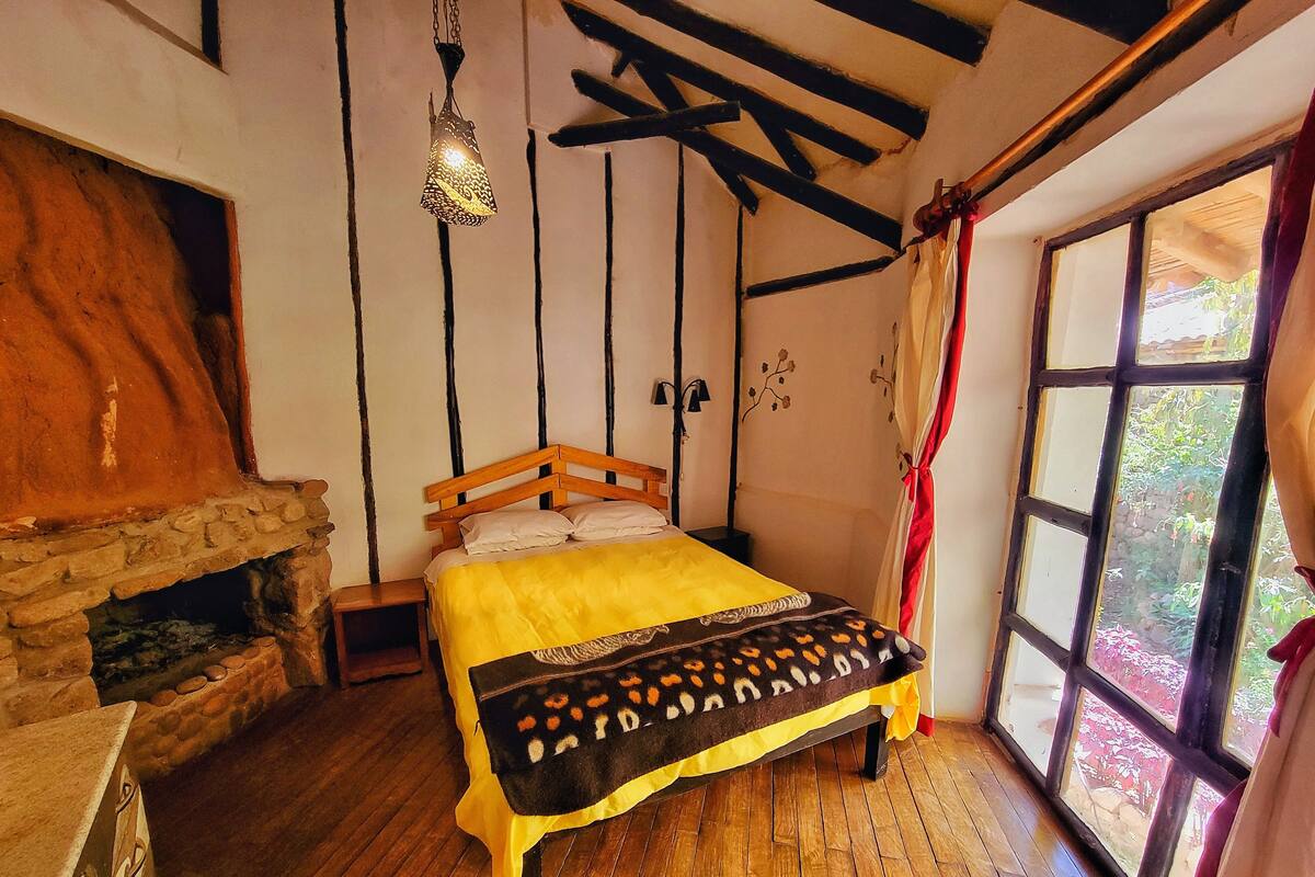 A bedroom with a wooden bed, a stone fireplace, and a large window with curtains.