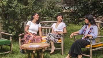 Three people sitting on wooden chairs in a garden with a round wooden table in the foreground.