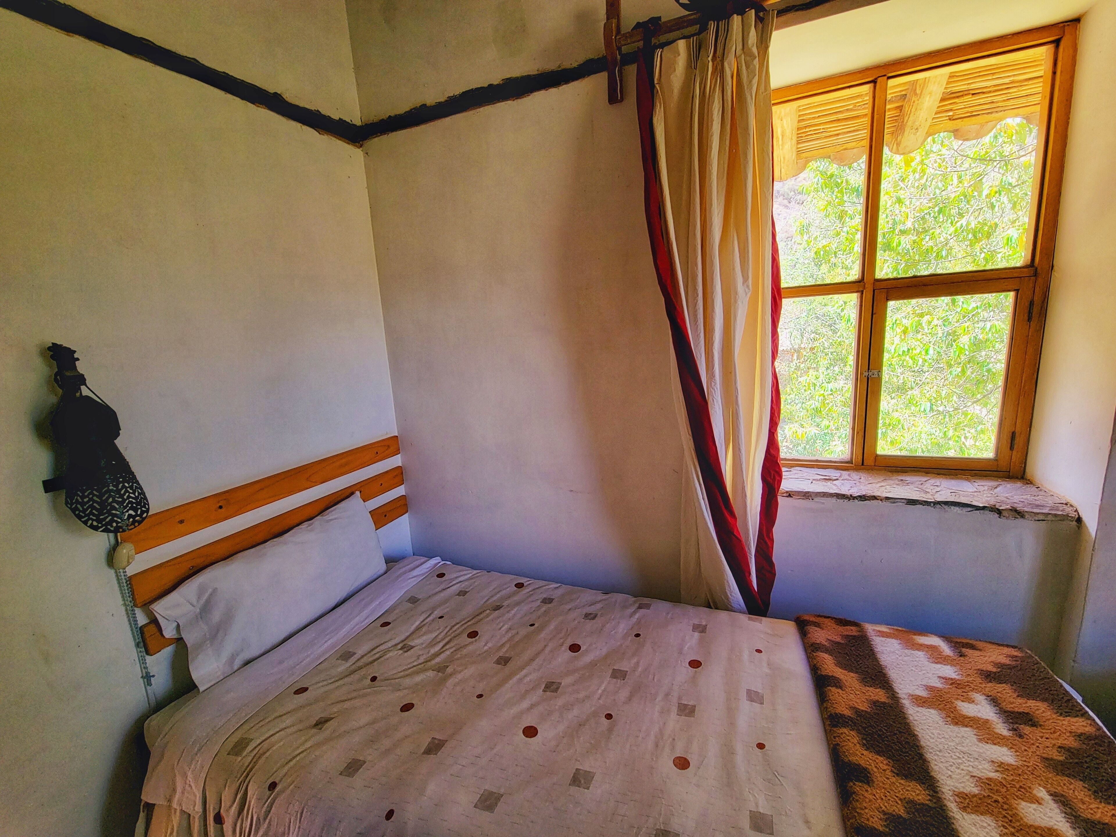A room with a bed, a window with curtains, and a wall-mounted light fixture.