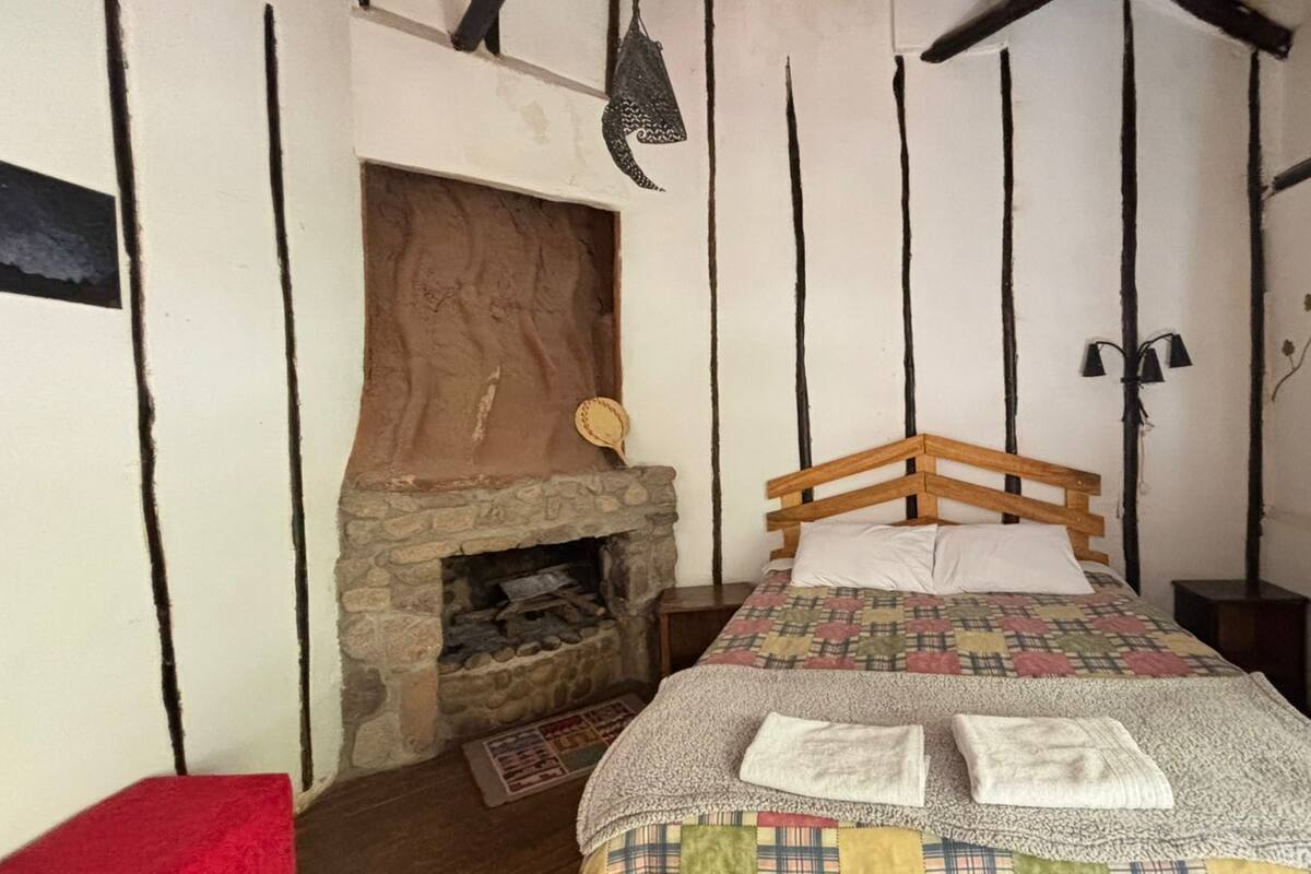 A bedroom with a stone fireplace, a wooden bed frame, and a quilted bedspread.