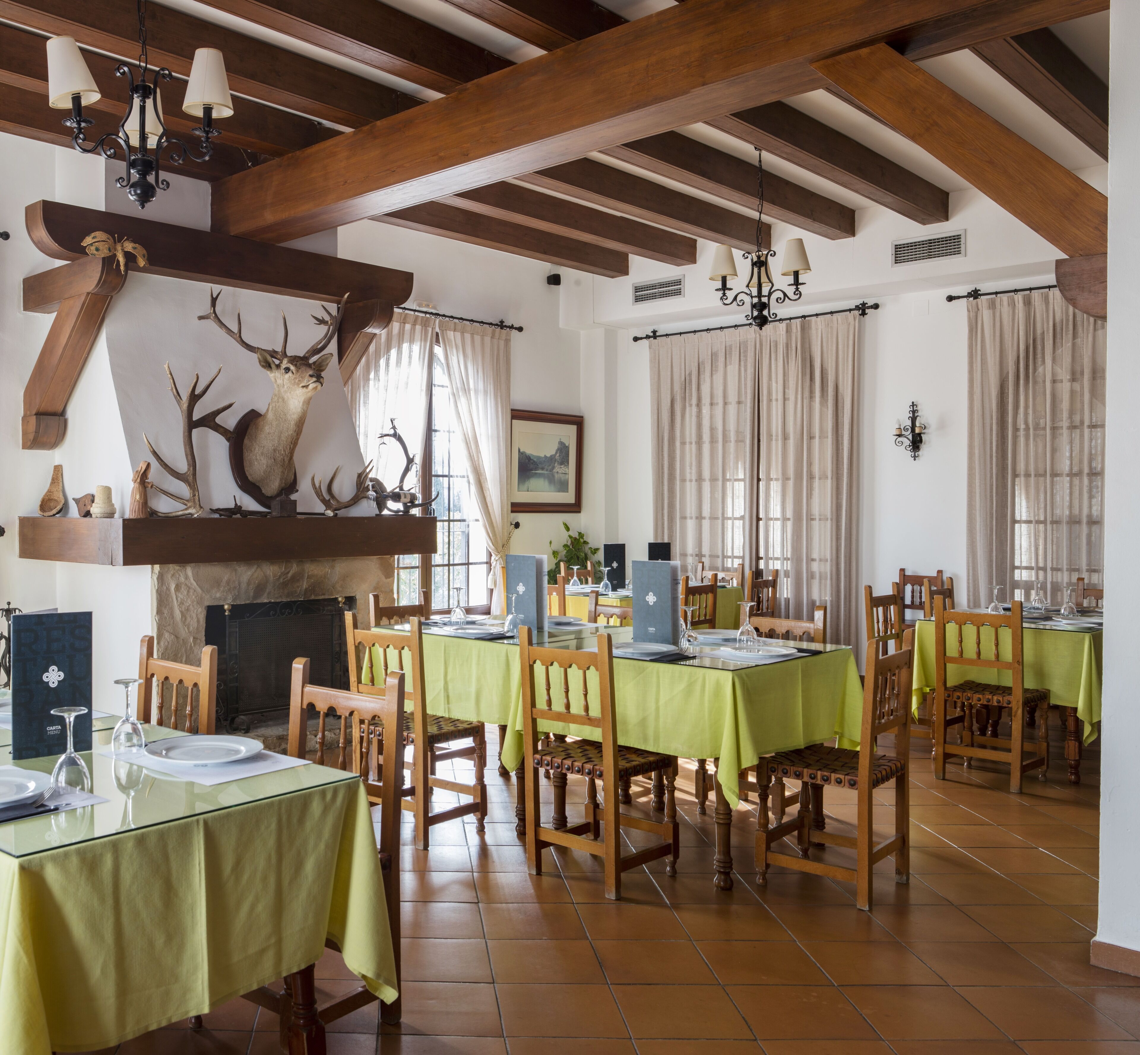 Un coin repas avec des tables et des chaises en bois, une cheminée et des bois de cerf accrochés au mur.