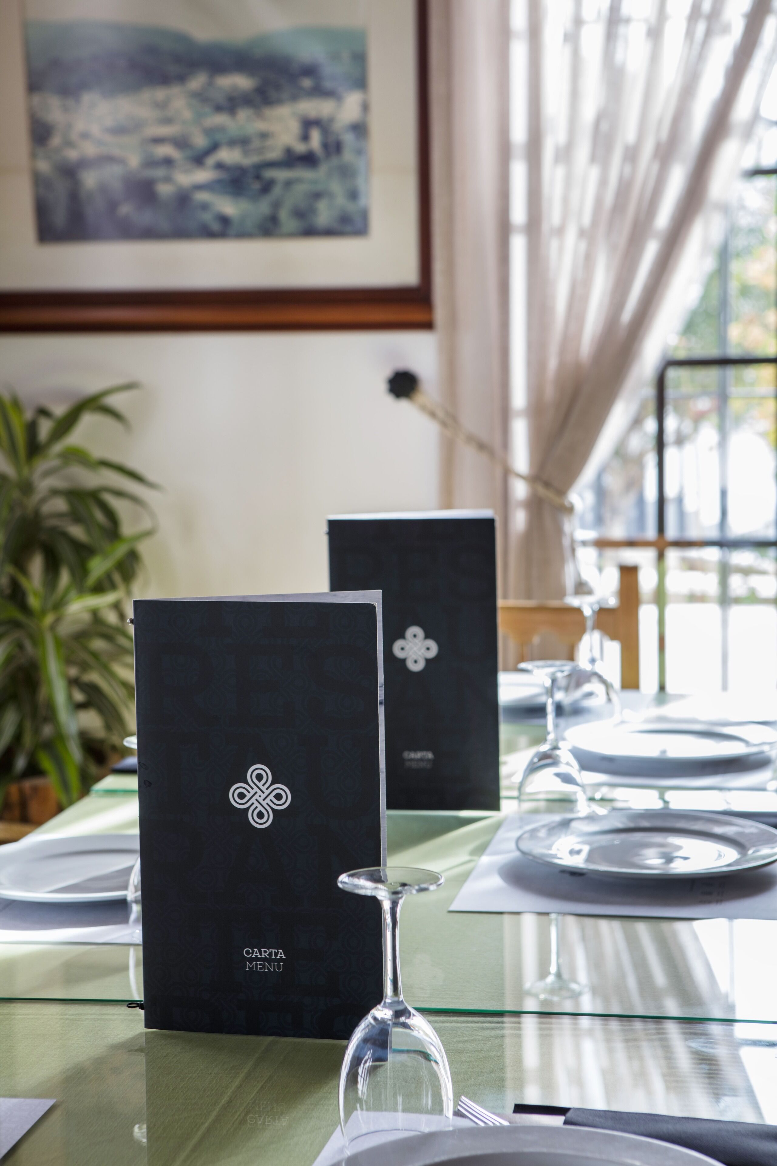 Une table dressée pour le repas, avec un menu, un verre à vin et une plante en pot.