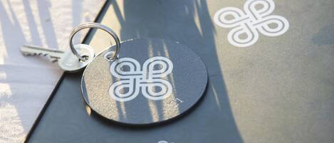 A metallic object with a circular emblem and a key ring, placed on a surface with a "CARTA MENU" label.