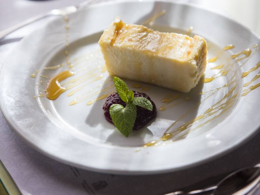 A dessert plate with a slice of cheesecake, a small berry, and a mint leaf, accompanied by a glass of red wine.