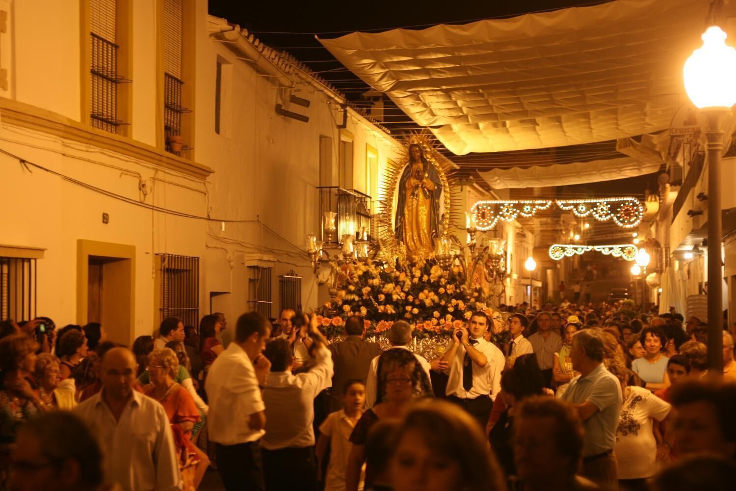 A crowded street scene with a large group of people gathered around a central display, possibly a religious or cultural event.
