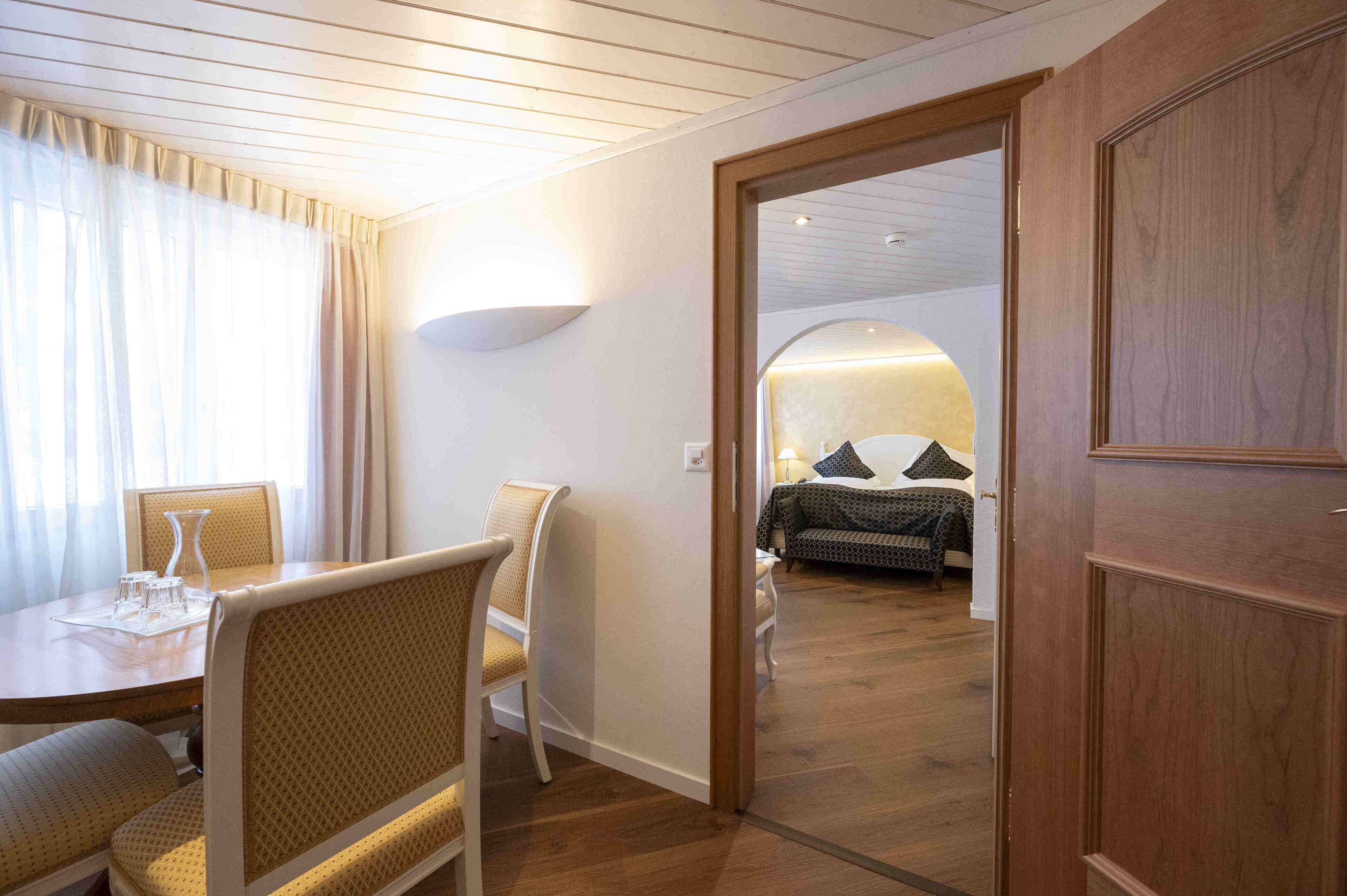 Une chambre d’hôtel avec un plancher en bois, un coin repas avec une table et des chaises, et un lit recouvert d’une couvre-lit à motifs.