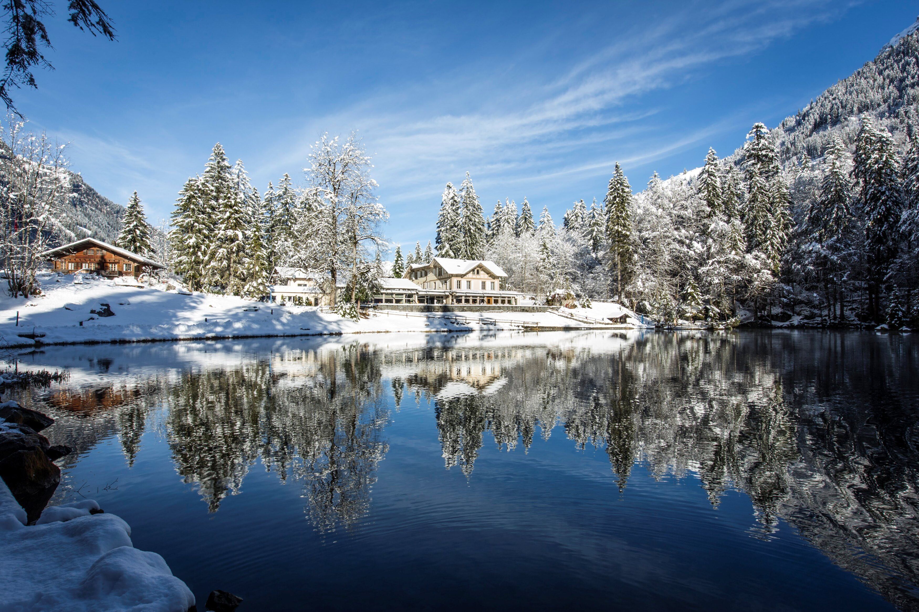 Un paysage enneigé avec un grand chalet et un lac paisible qui reflète les arbres et les bâtiments.