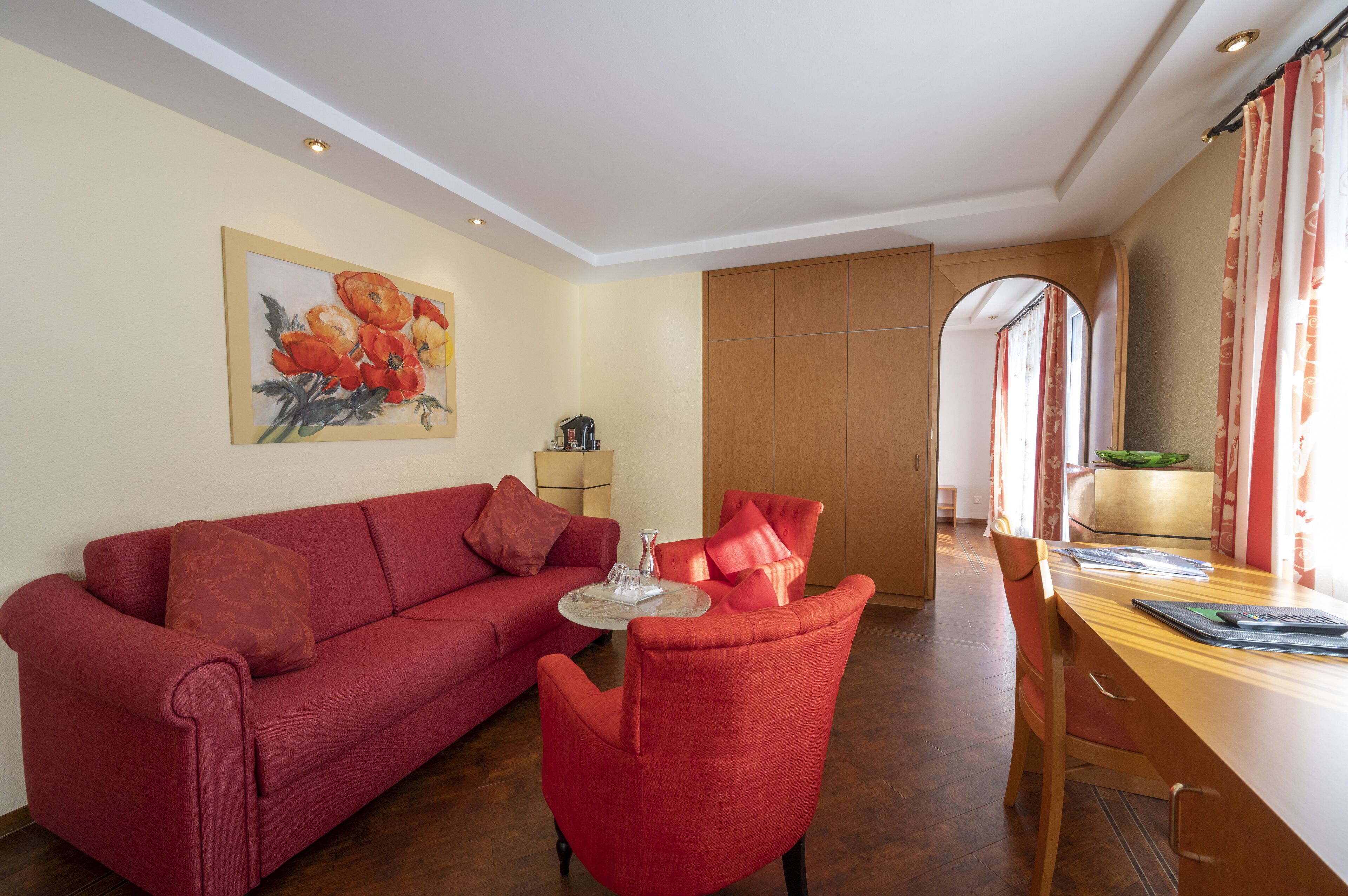 A living room with a red sofa, a matching armchair, a coffee table, and a dining area with a wooden table and chairs.