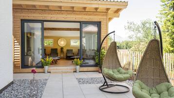 A modern house with a wooden exterior, large glass doors leading to a living area with a sofa and a hanging chair.