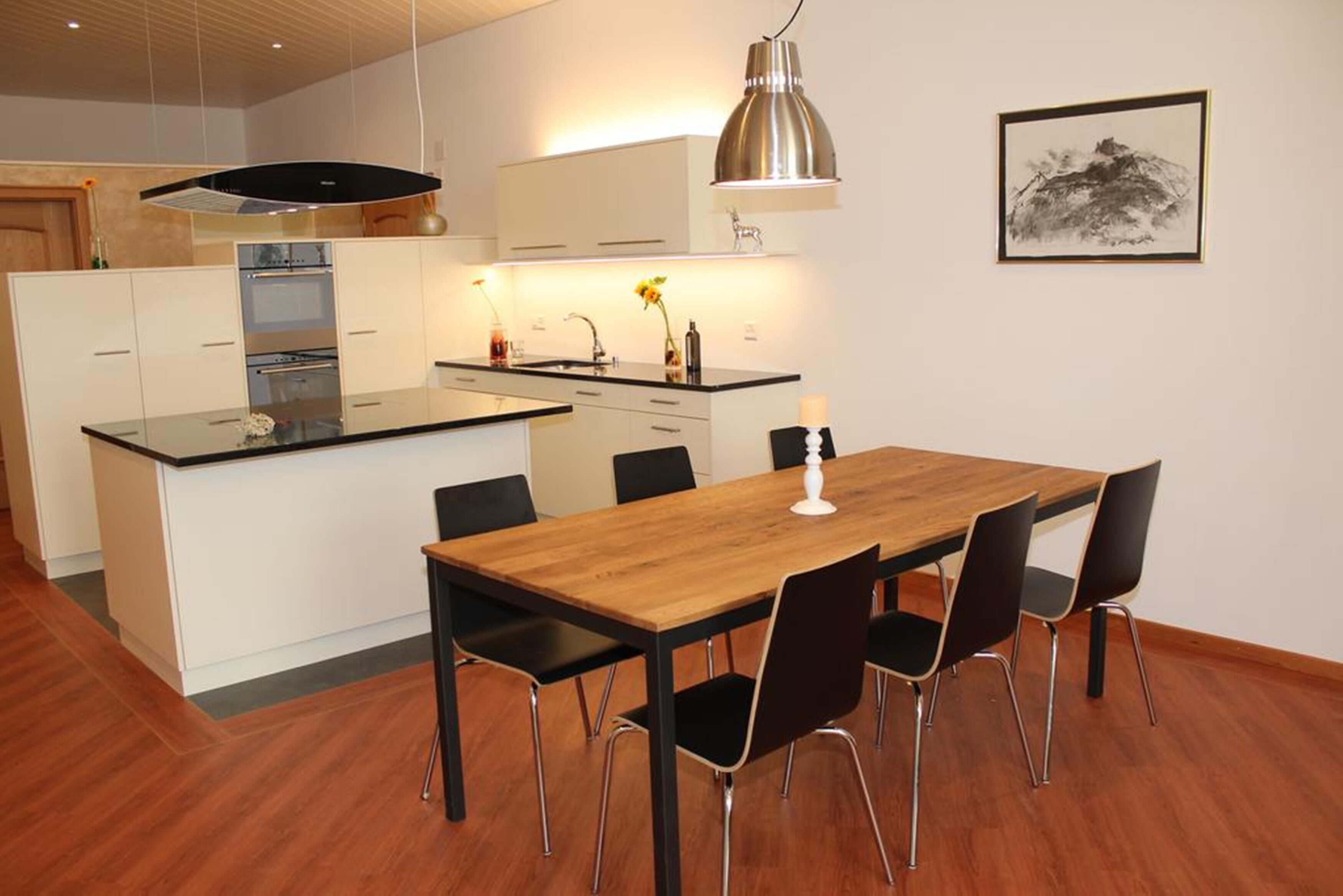 Een moderne keuken met witte kastjes, een houten eettafel en zwarte stoelen.