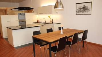 Een moderne keuken met witte kastjes, een houten eettafel en zwarte stoelen.