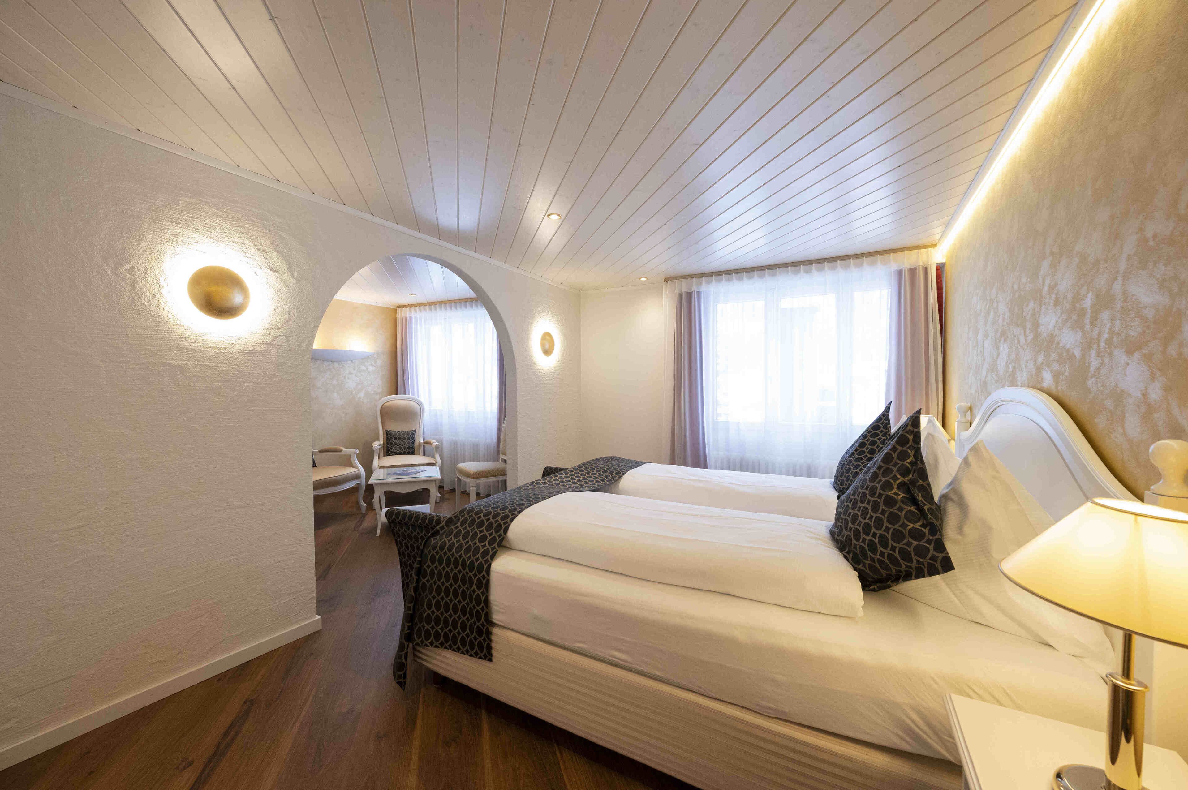 A hotel room with a large bed, a chair, a desk, and a lamp.