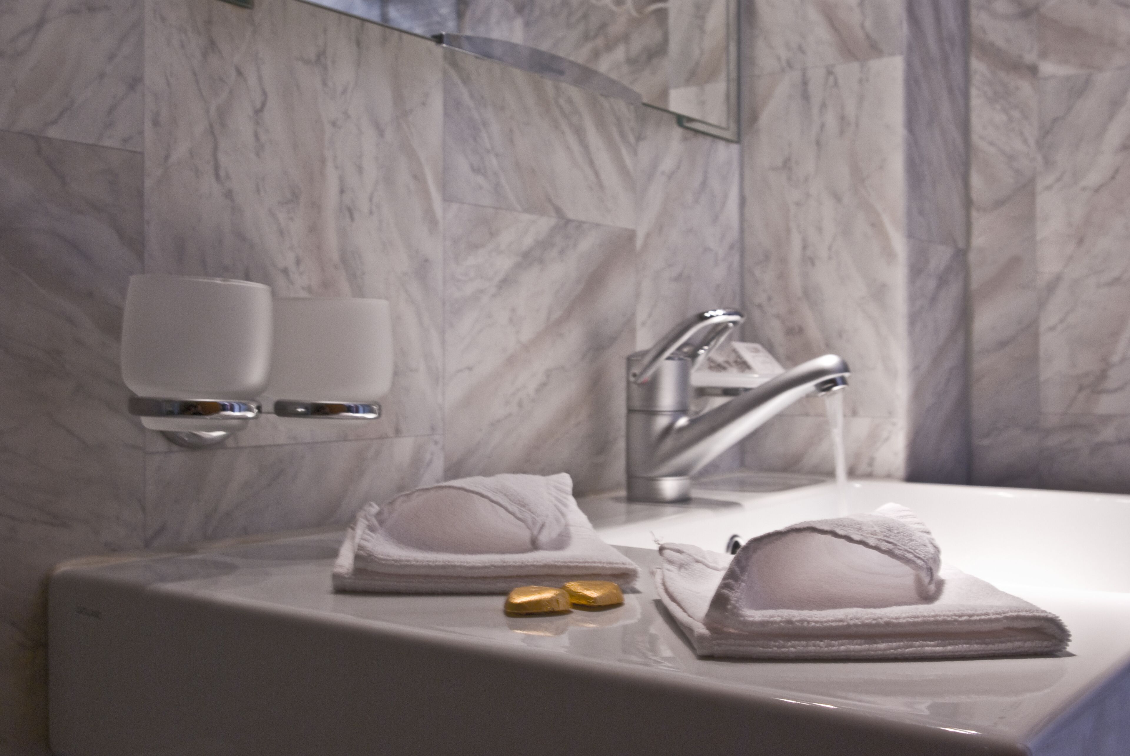 A bathroom with a marble wall, a sink with two gold soap bars, and a towel folded on the counter.