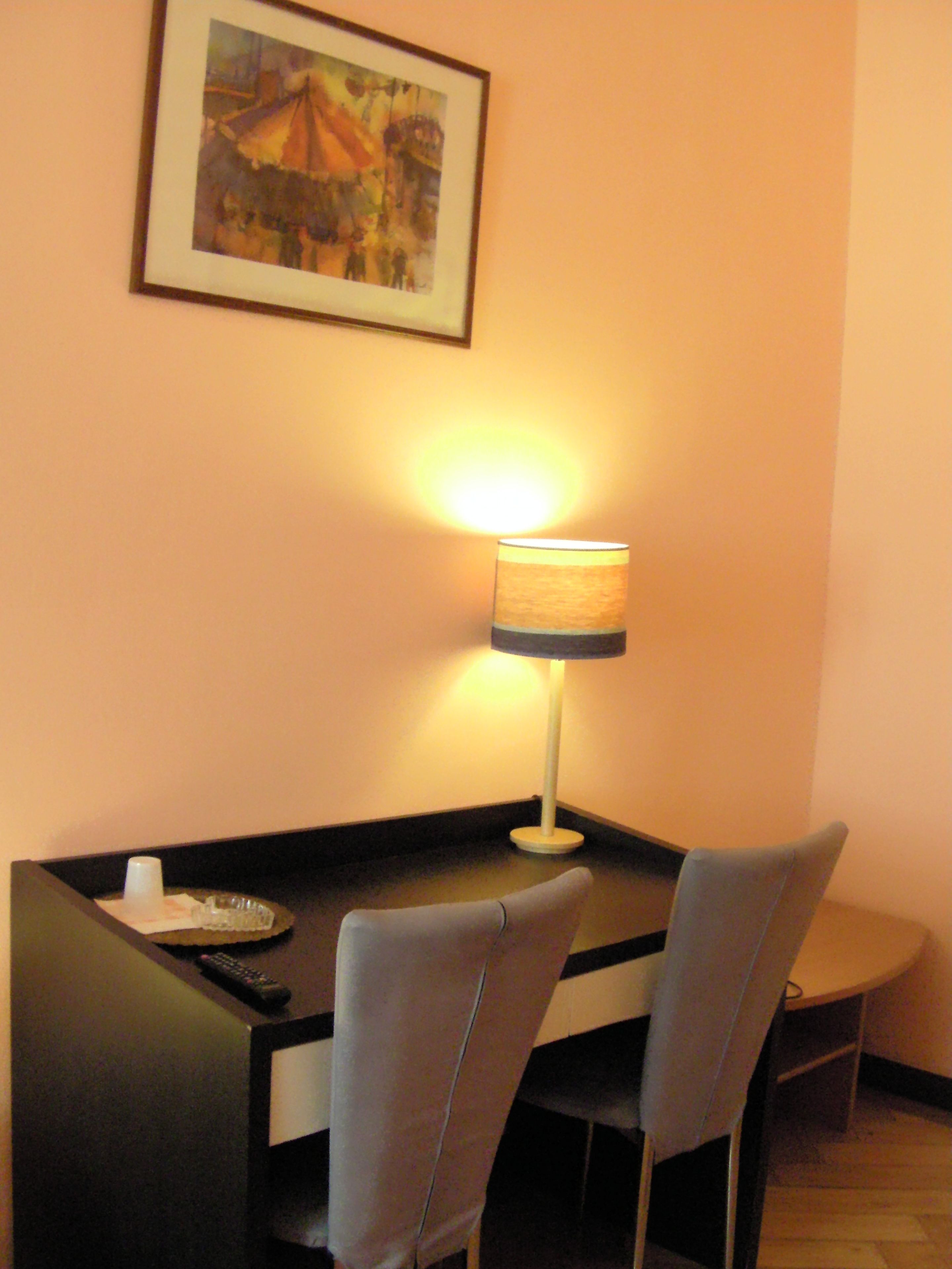 Un rincón comedor íntimo con una mesa, dos sillas, una lámpara y un cuadro en la pared.
