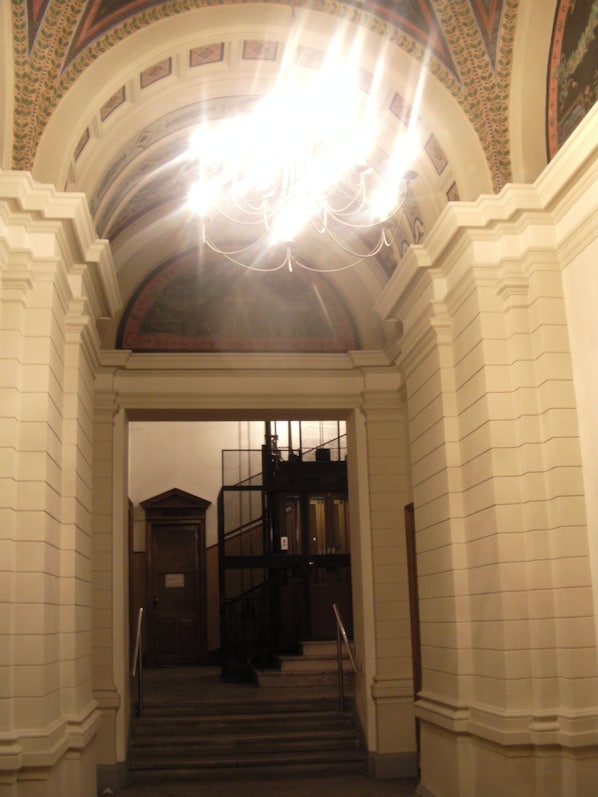 A grand staircase with a chandelier, leading to a dark staircase.