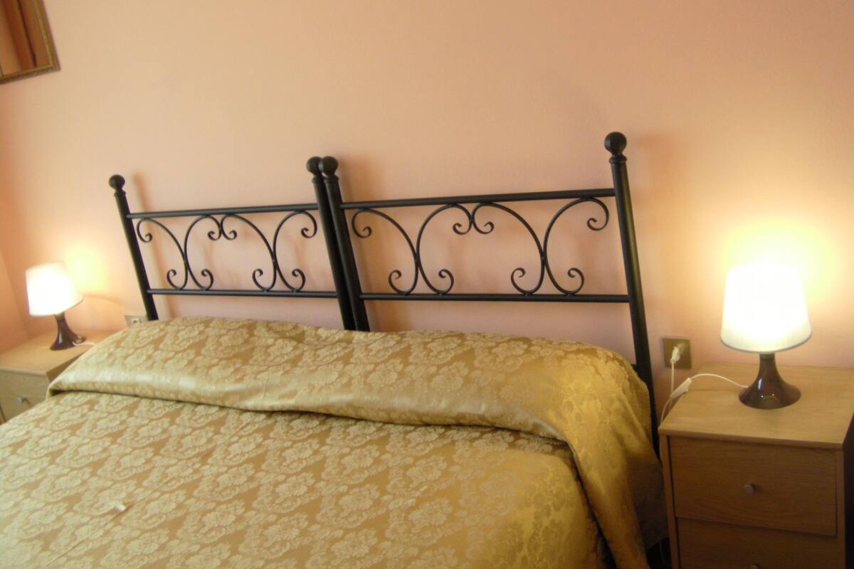 A bed with a patterned bedspread, a metal headboard, and two bedside lamps on wooden nightstands.