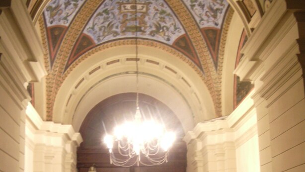 A grand arched doorway with a chandelier, flanked by white tiled walls and a detailed ceiling mural. - Alla Stazione (Trieste)