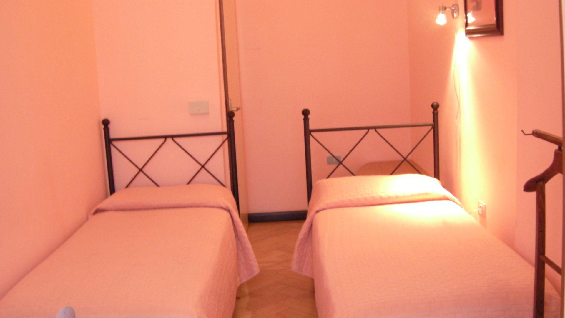 A room with two single beds, a wooden door, and a wall-mounted light fixture.