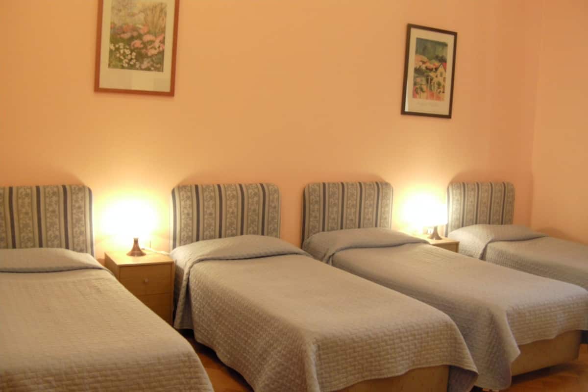 A hotel room with four single beds, each with a headboard and bedside table.