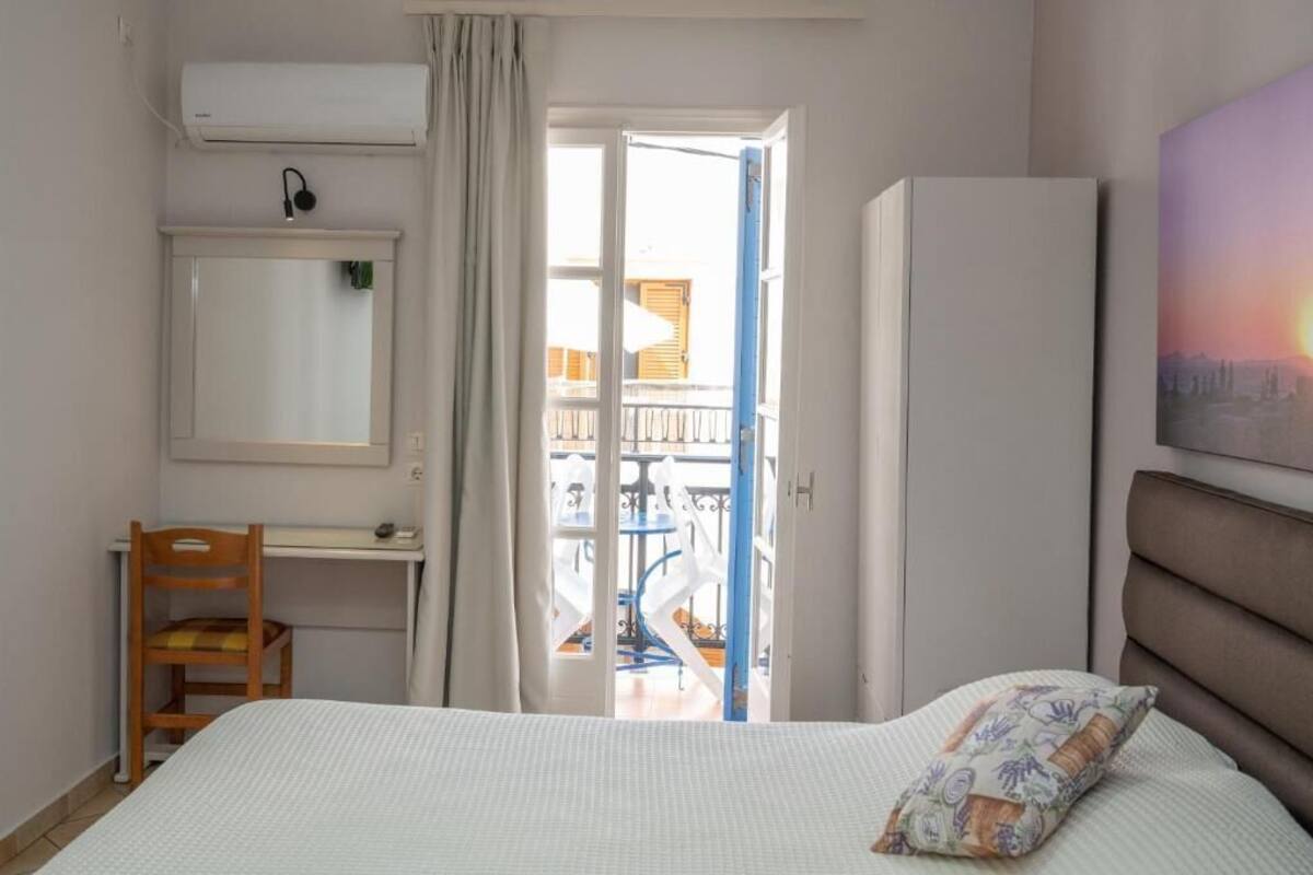 Un dormitorio con cama, escritorio, silla, aire acondicionado, armario y balcón con mobiliario exterior.
