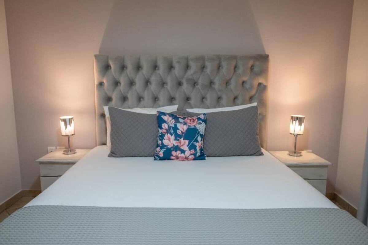 Una cama bien hecha con cabecera capitonada, dos lámparas de noche y un cojín estampado.