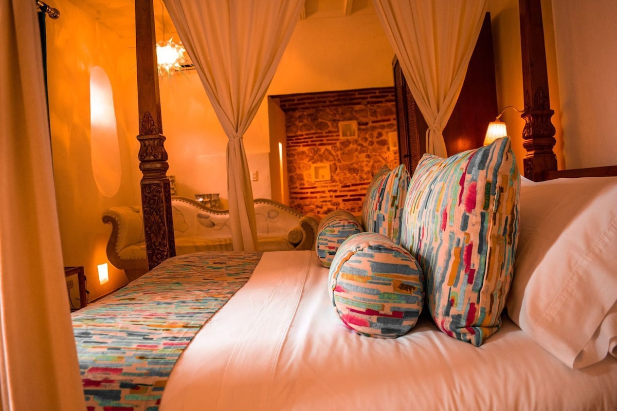 Ein Bett mit einem gemusterten Bettbezug, Kissen mit Streifen und eine Steinwand im Hintergrund.