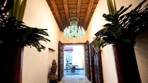 A hallway with a chandelier, potted plants, and a statue.