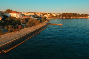 Uma vila costeira com casas à beira-mar, um cais e céu claro.