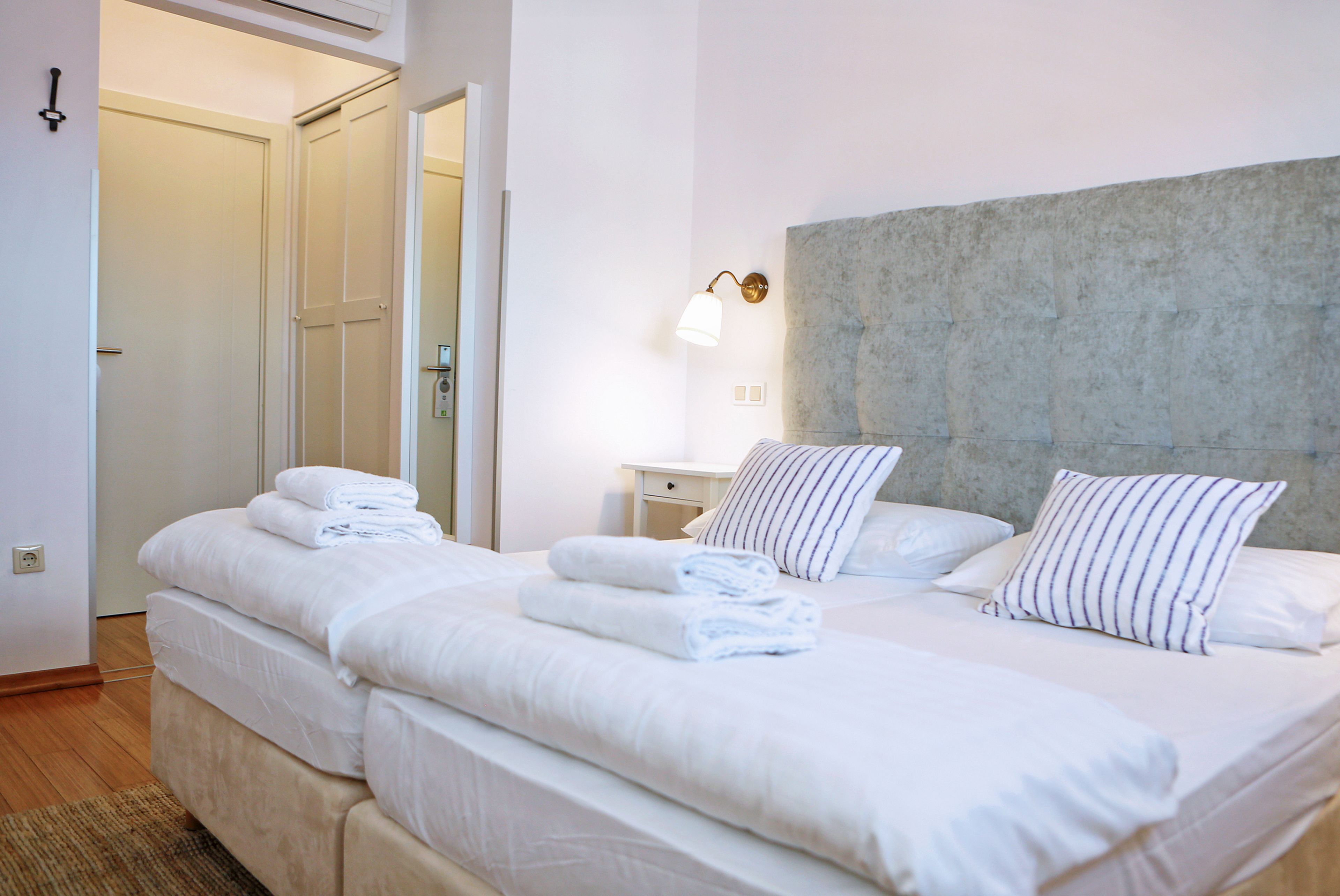 Habitación de hotel con una cama grande, una mesita de noche, una lámpara y una puerta que da a otra habitación.