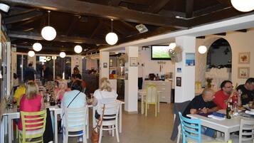 A restaurant with wooden beams, hanging lights, and a TV screen.