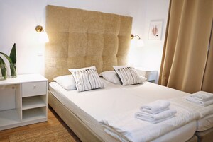 A neatly made bed with white linens and striped pillows, a bedside table with a lamp, and a wall-mounted light fixture.