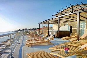 Una terraza con tumbonas de madera, barandilla de cristal y vistas al mar.