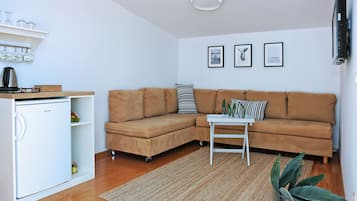 Una sala de estar con un sofá marrón, una mesa de centro blanca, un refrigerador blanco y una planta.