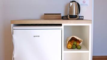 Una kitchenette compacta con un refrigerador blanco, una cafetera y una estante con tazas.