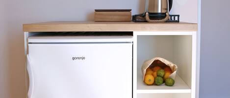 A compact kitchenette with a white refrigerator, a coffee maker, and a shelf with mugs.
