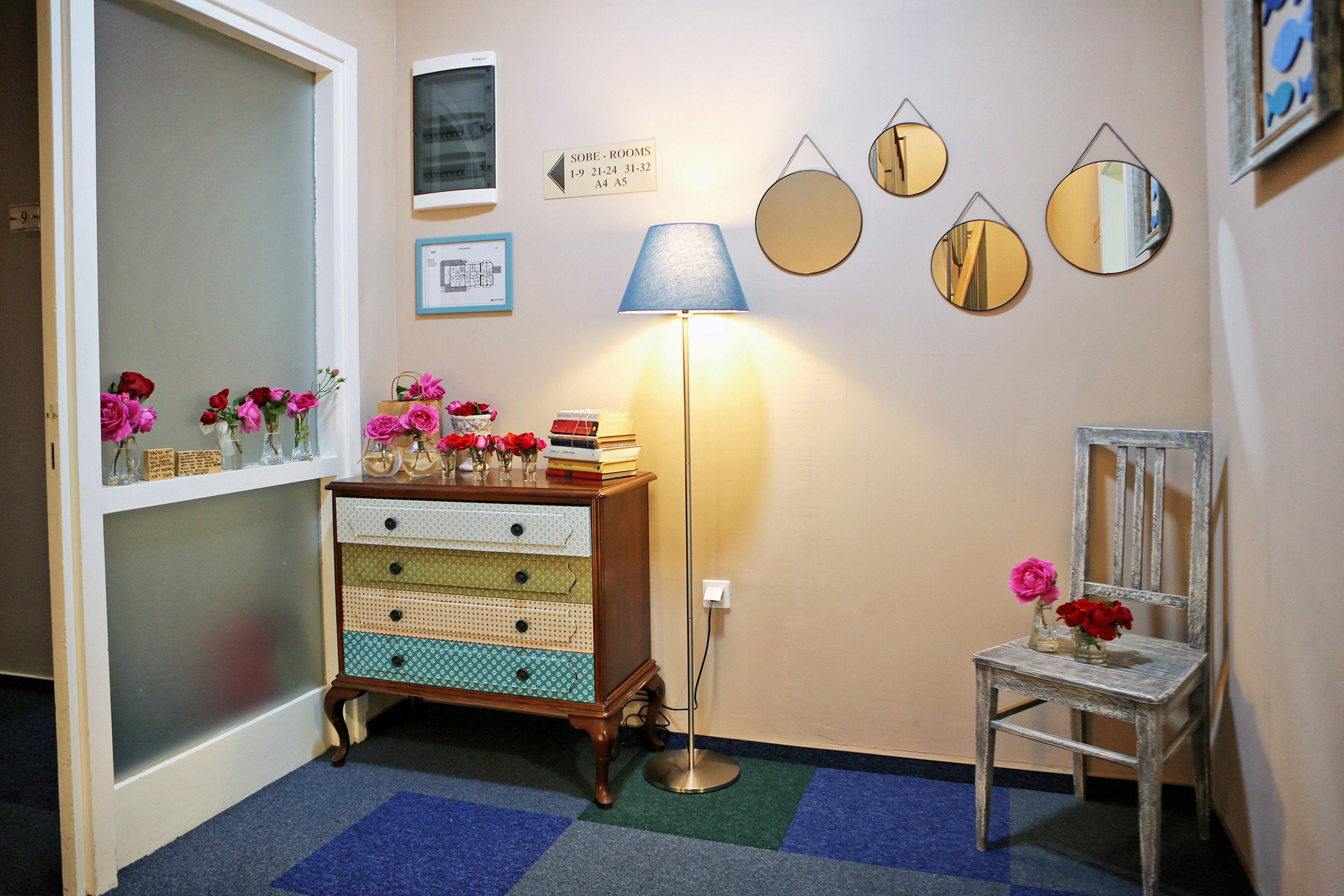 A hallway with a vintage-style dresser, a lamp, and a chair with flowers.