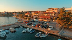 A marina with boats docked, a parking area with cars, and buildings with balconies overlooking the water. - Hotel Delfin (Zadar)