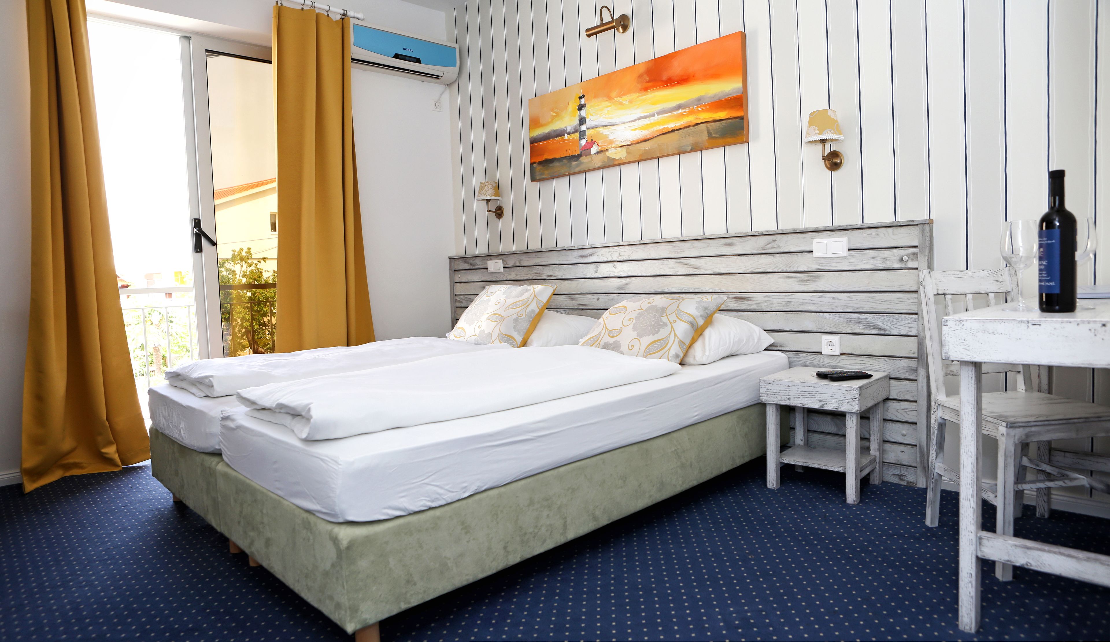 Habitación de hotel con una cama, una mesita, un cuadro en la pared y una botella de vino sobre la mesa.