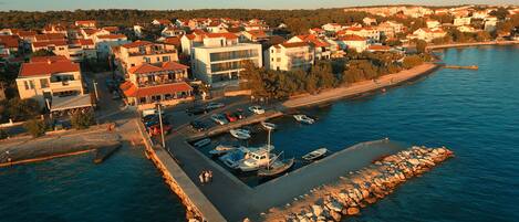 An aerial view of a coastal town with a marina, buildings, and a rocky breakwater.