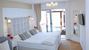 A bedroom with a large bed, a bedside table with a lamp, a grey sofa, and a TV on the wall. - Hotel Delfin (Zadar)