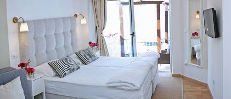 Een slaapkamer met een groot bed, een nachtkastje met een lamp, een grijze bank en een televisie aan de muur.