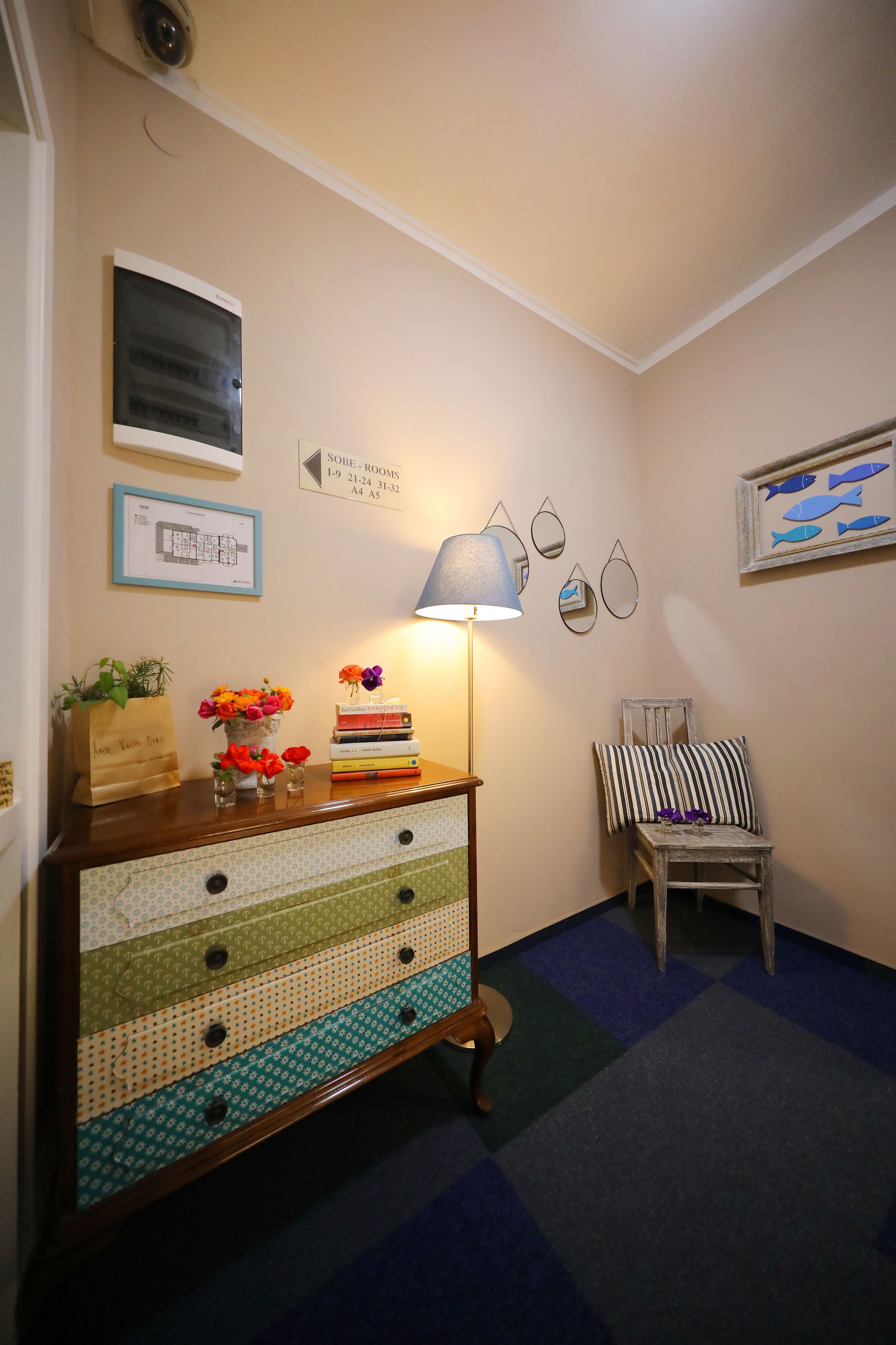 A room with a wooden dresser, a lamp, a chair, and a wall with a fish-themed picture.