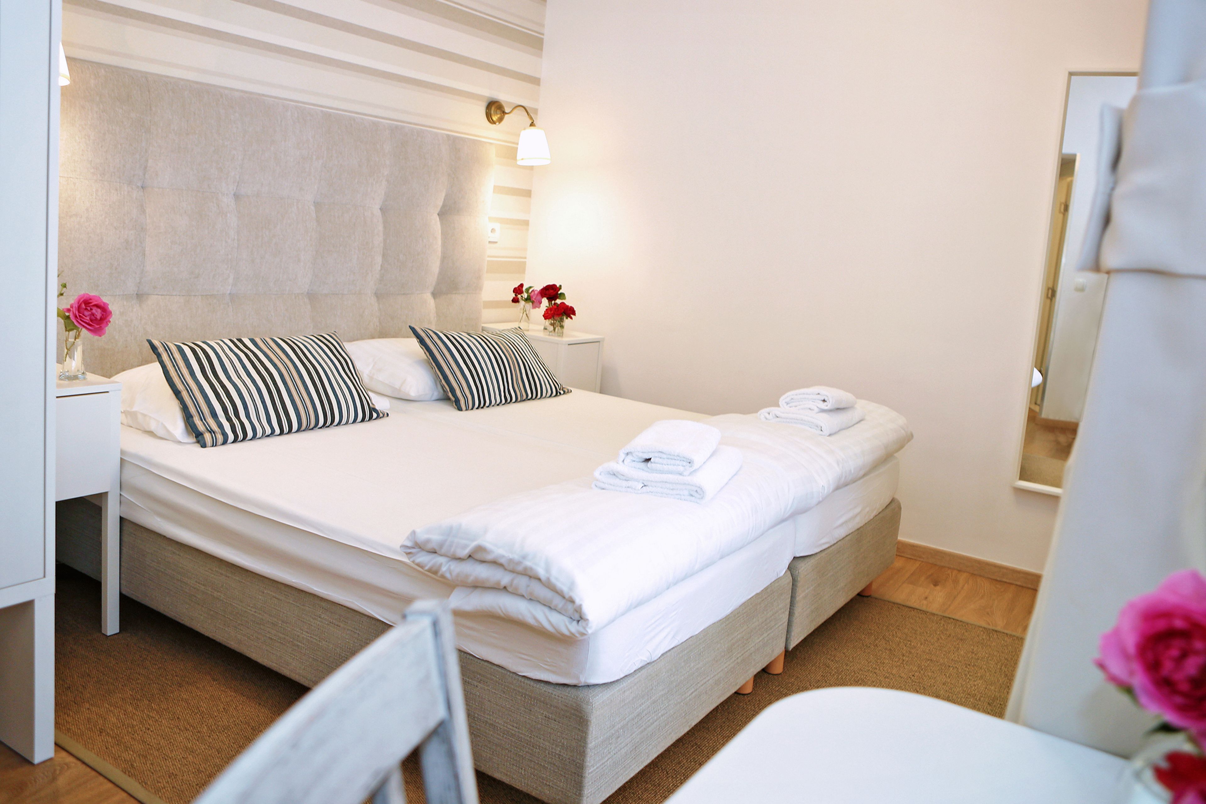 A double bed with a tufted headboard, a bedside table with a vase of flowers, and a nightstand with a lamp.