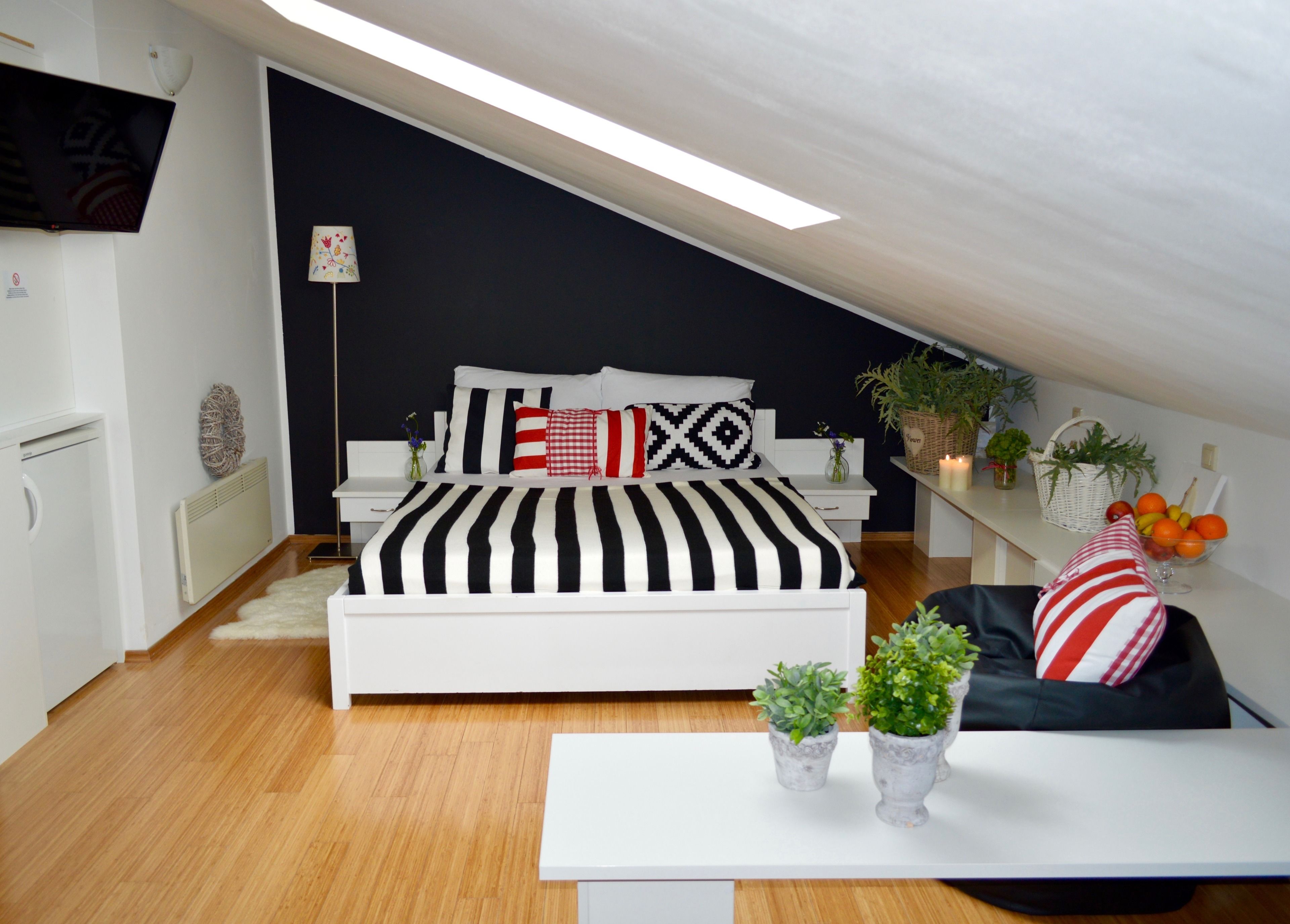 A modern bedroom with a bed, bedside tables, a desk, and potted plants.