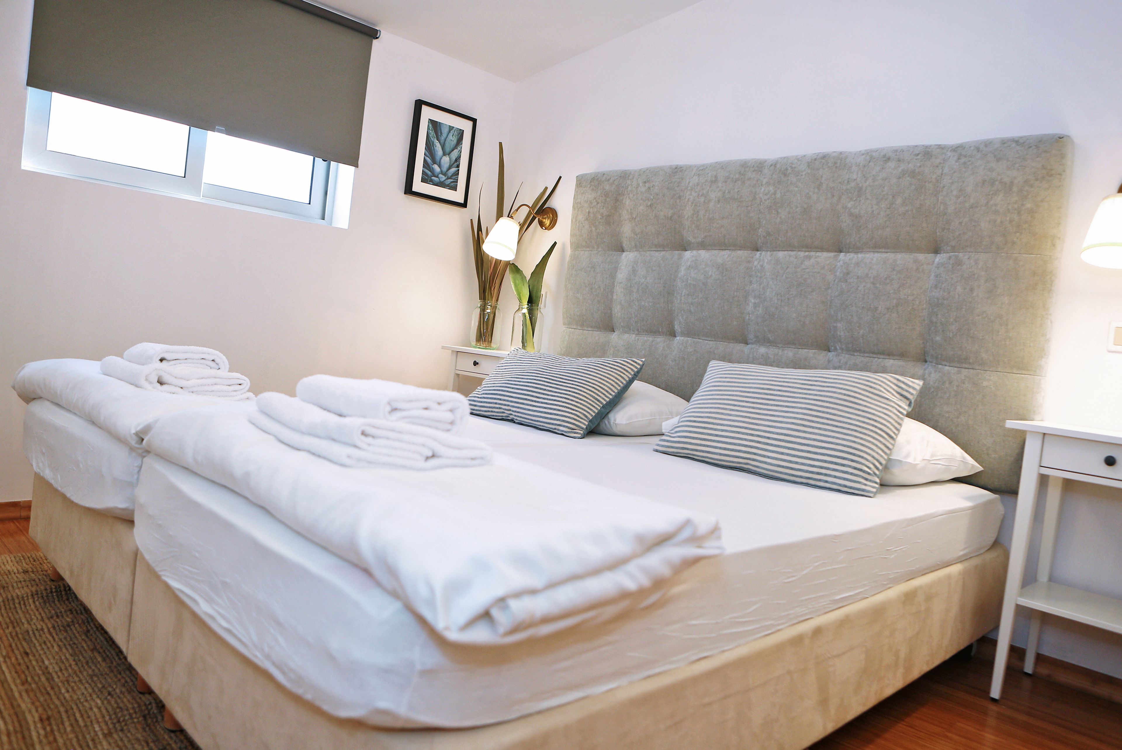 Habitación de hotel con una cama grande, dos mesitas de noche, una ventana con persianas y un cuadro colgado en la pared.