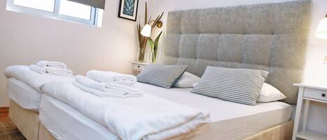 A hotel room with a large bed, two bedside tables, a window with blinds, and a wall-mounted picture.