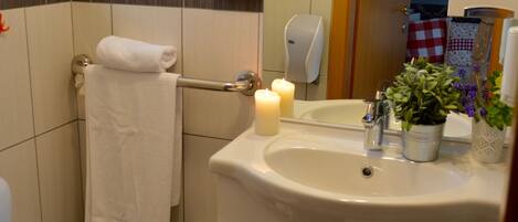A bathroom with a toilet, sink, mirror, towel rack, and a small wooden stool.